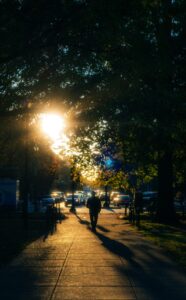 Homem caminhando em calçada ensolarada com árvores ao redor, representando os benefícios da caminhada matinal
