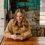 mulher sentada olhando para o celular, representando o cuidado com a saúde mental no Dia Mundial da Saúde Mental